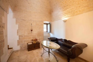 A cozy room with a stone wall, a leather sofa, a small table, and a wooden cabinet with flowers.