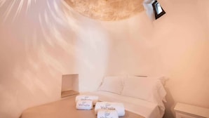 Een slaapkamer met een bed, twee handdoeken met 'WePuglia'-branding, een bedlamp en een witte muur.
