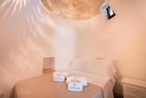 A bedroom with a bed, two towels with 'WePuglia' branding, a bedside lamp, and a white wall. - WePuglia - Trullo Sentimento (Martina Franca)