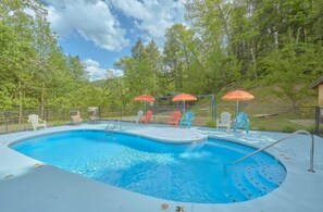 Piscina com prancha de mergulho, rodeada por árvores e mobiliário de exterior.