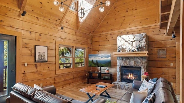 A wooden cabin interior with a fireplace, leather furniture, a television, and a stone accent wall. - 5 bdrm MT view, 10 mins DT,Hot Tub (Gatlinburg)