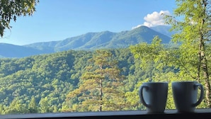 A view of a mountain range with lush greenery, two white cups on a railing, and a clear sky. - 5 bdrm MT view, 10 mins DT,Hot Tub (Gatlinburg)