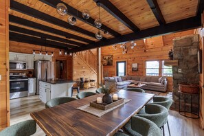 A wooden interior with a dining table, chairs, a kitchen with appliances, and a living area with a sofa.