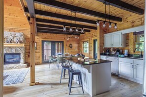 A spacious kitchen with a central island, wooden beams, and a stone fireplace.