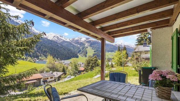 Pátio com mesa e cadeiras, vista para uma paisagem montanhosa.