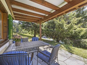 Un patio couvert avec une table et des chaises, une vue sur une zone boisée et un chemin en pierre.