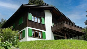 Um chalé de dois andares com telhado inclinado, persianas verdes e uma varanda.