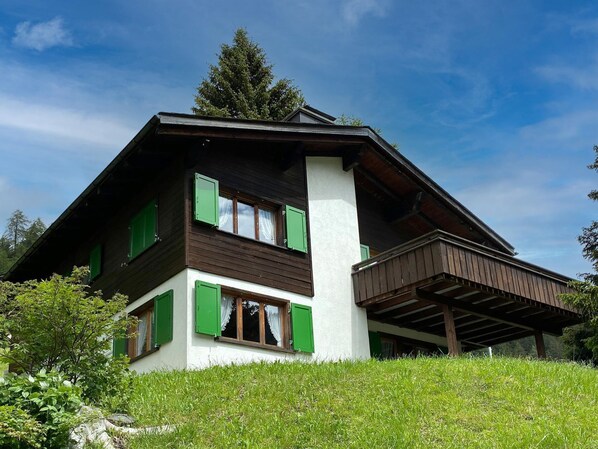Un chalet à deux étages, doté d’un toit en pente, de volets verts et d’un balcon.