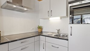 Cozinha moderna com armários brancos, pia de aço inoxidável e forno embutido.