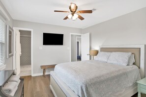 Un dormitorio con cama, ventilador de techo, televisor y vestidor.