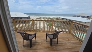 Une terrasse en bois avec deux chaises donnant sur l’océan, une rambarde en bois et une vue sur la plage et les maisons.