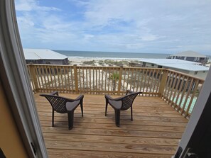 A wooden deck with two chairs facing the ocean, a wooden railing, and a view of the beach and houses.