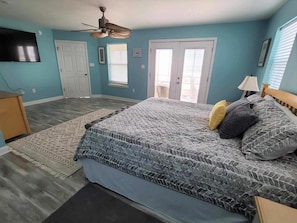 A bedroom with a bed, a ceiling fan, a TV, and a door.