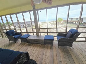 A covered outdoor seating area with wicker furniture and a view of the beach.
