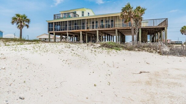 Une maison située en bord de mer, dotée d’un balcon, de palmiers et d’une plage de sable.