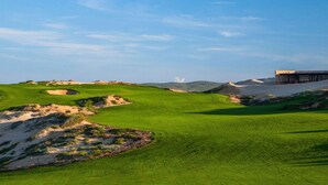 Un parcours de golf avec des bunkers de sable, un club-house et un ciel dégagé.