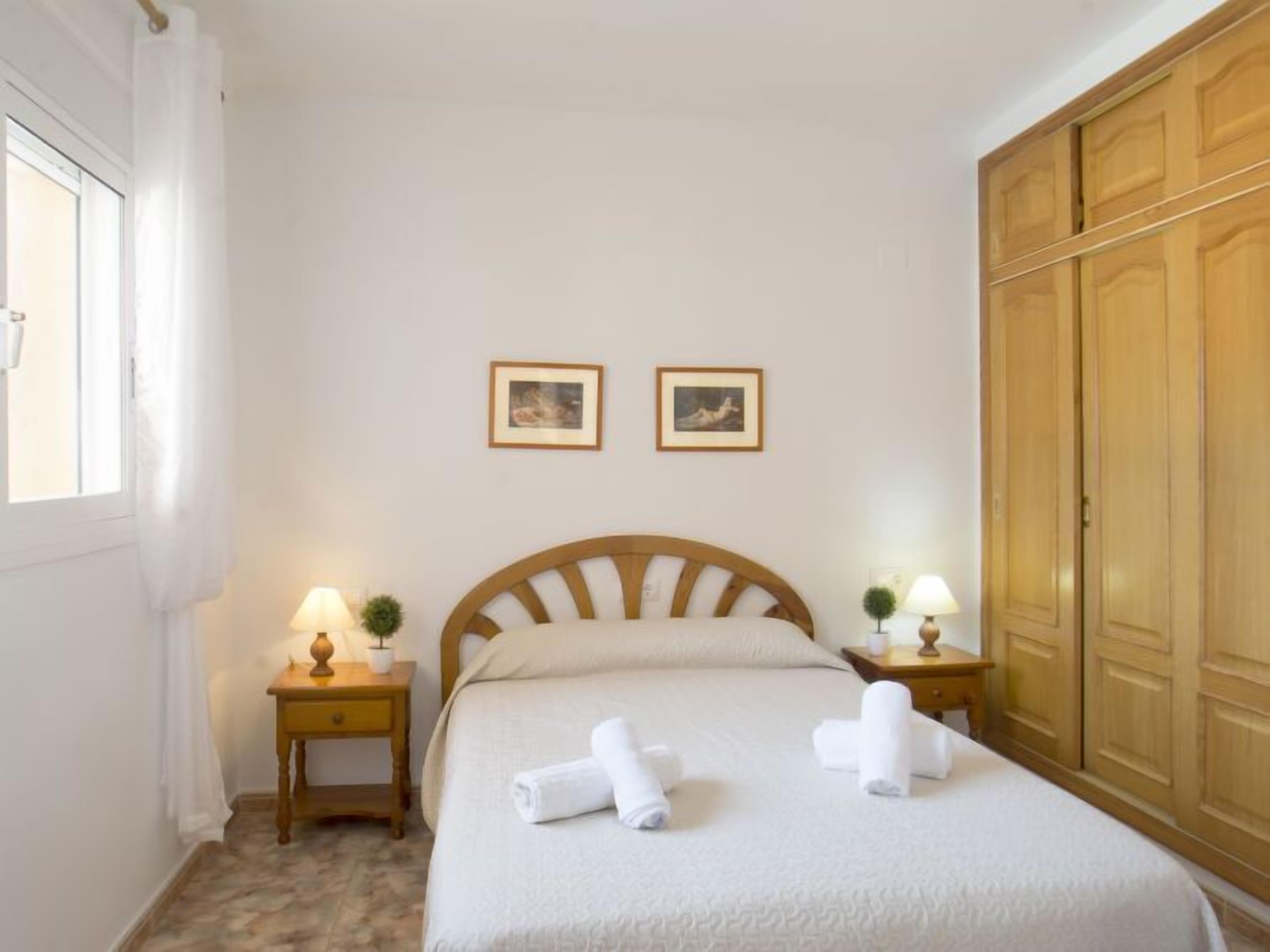Une chambre à coucher bien rangée, avec un lit, deux tables de chevet dotées de lampes, une armoire et deux tableaux encadrés accrochés au mur.