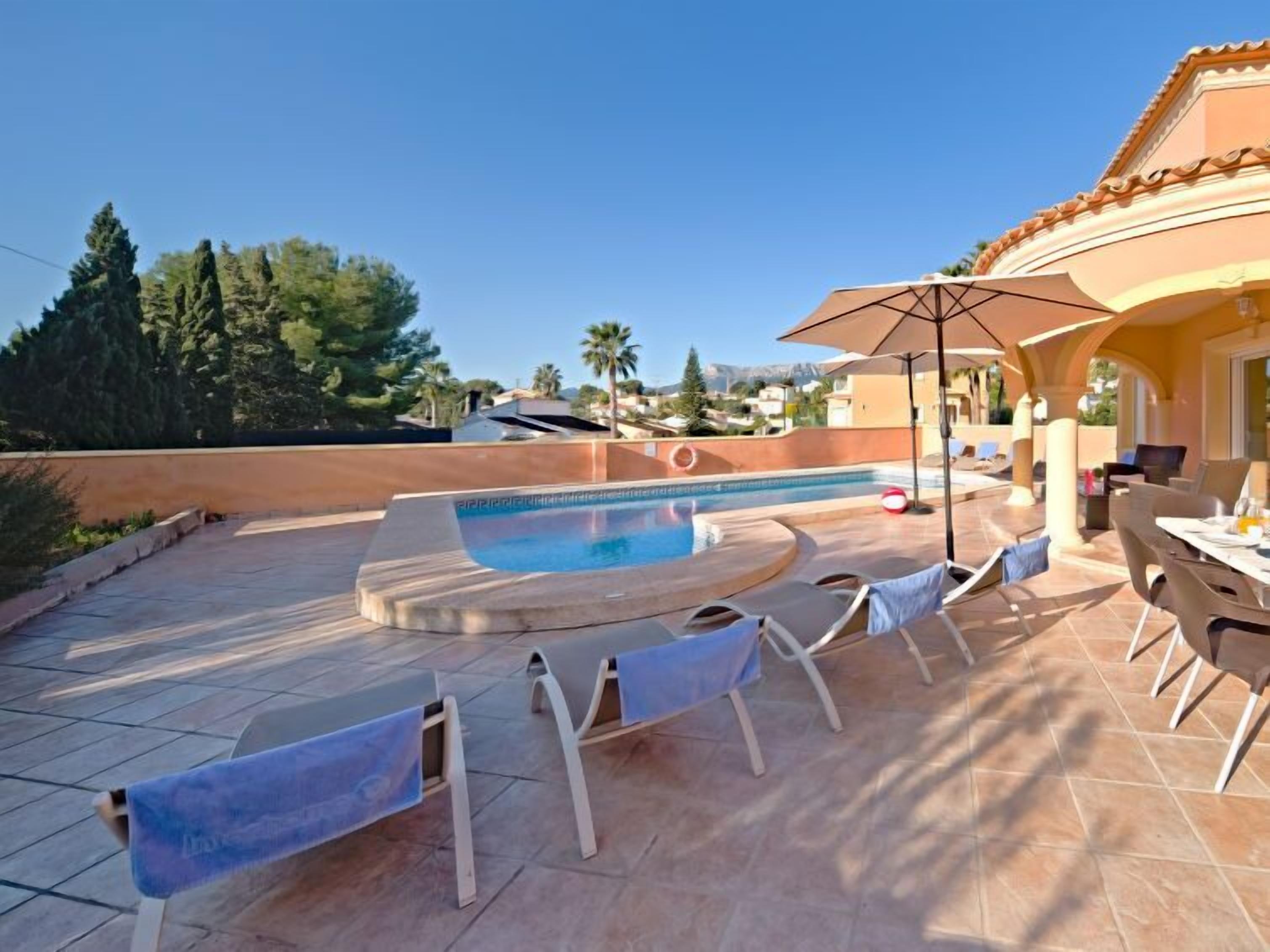 A pool area with a hot tub, lounge chairs, and a table with umbrellas.
