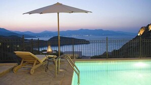 A pool with a view of the sea and mountains, a lounge chair, and an umbrella. - Istron Collection Villas (Lasithi)