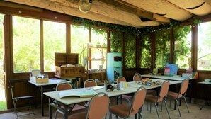 Un aula rústica con mobiliario de madera, ventanas amplias y abundante vegetación.