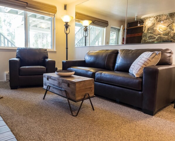 A living room with a leather sofa, a wooden coffee table, and two floor lamps. - Winter Park Basecamp for Adventure (Winter Park)