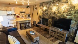 Uma sala de estar moderna com uma parede de destaque em pedra, uma TV de tela plana e uma área de estar aconchegante com sofás de couro.