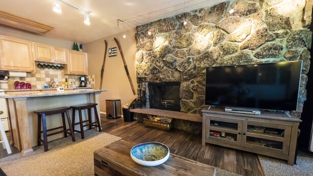 Uma sala de estar acolhedora com lareira de pedra, uma televisão e uma mesa de centro de madeira.