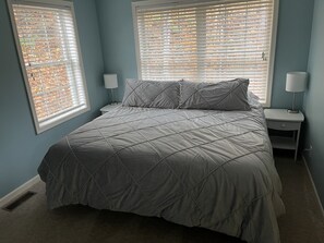 A bedroom with a bed, two bedside tables, and a window with blinds.