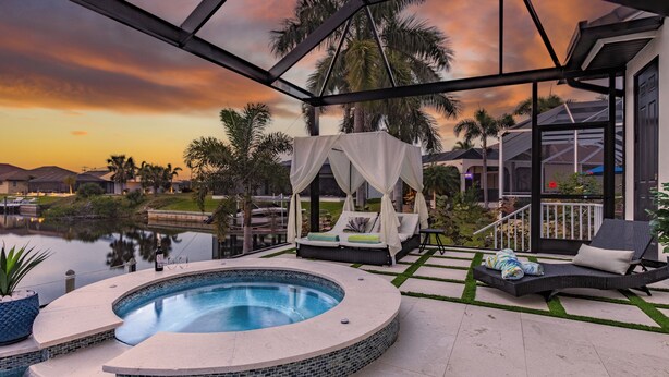 Uma banheira de hidromassagem com toldo, cadeiras de sol e vista para uma área residencial ao pôr do sol.