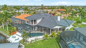Uma casa moderna com uma piscina grande, protegida por vidro, rodeada por palmeiras e um gramado bem cuidado.