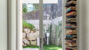 A hallway with a glass door leading to a garden, a marble floor, and a tall stack of books on a stand. - Vista Unica Sulle Isole (Baveno)