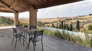 An outdoor patio with a table and chairs, overlooking a scenic landscape with hills and a swimming pool.