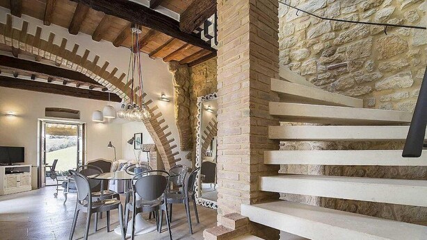 A modern interior with a stone wall, a staircase, and a dining area with chairs and a table.