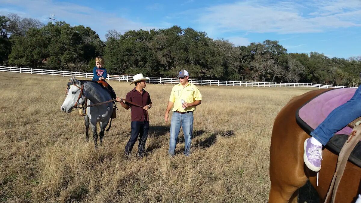 Une personne à cheval dans un champ verdoyant, avec une clôture blanche en arrière-plan.