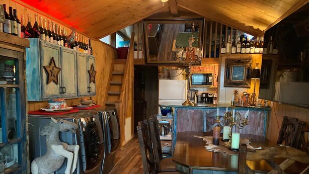 Een rustiek interieur met houten wanden, een eettafel met stoelen en een bar met flessen.