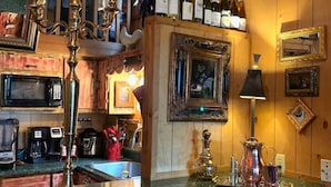 Een barruimte met houten lambrisering, een aanrecht met een collectie wijnflessen, een decoratieve lamp en een barstoel in vintage-stijl.