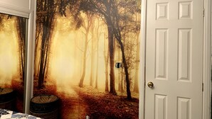 A room with a forest-themed wall mural, a white door, and a wicker basket.