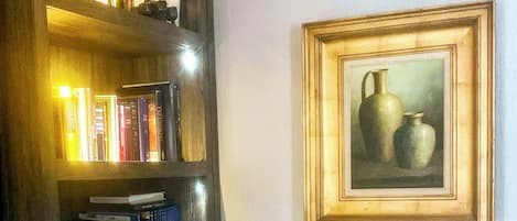 Una estantería con libros y objetos decorativos, y un cuadro enmarcado de jarrones en la pared.
