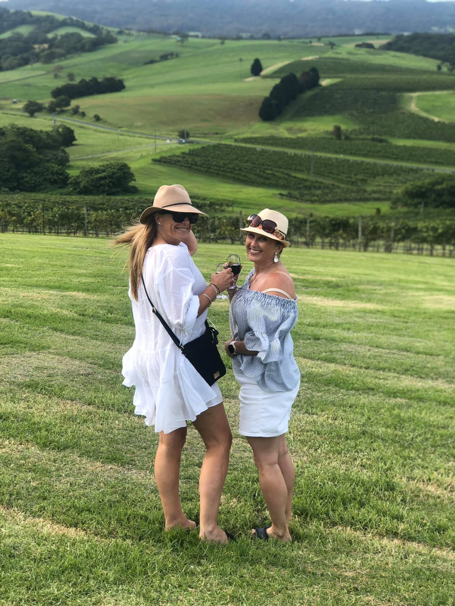 Two people standing on a grassy field with a hilly landscape in the background.