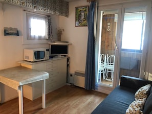 Compact room with a kitchenette, dining table, sofa, and window with a curtain.