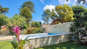 Una piscina de piedra con un muro de piedra, rodeada de un césped cuidado y varios árboles.