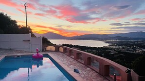 A swimming pool with a pink flamingo float, a stone-tiled deck, and a view of a body of water and mountains during sunset. - 3 bedroom Villa in Porticcio with Sea view (PORTICCIO)