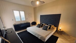 A modern bedroom with a large bed, a black desk, a window with a city view, and a textured wall. - 3 bedroom Villa in Porticcio with Sea view (PORTICCIO)