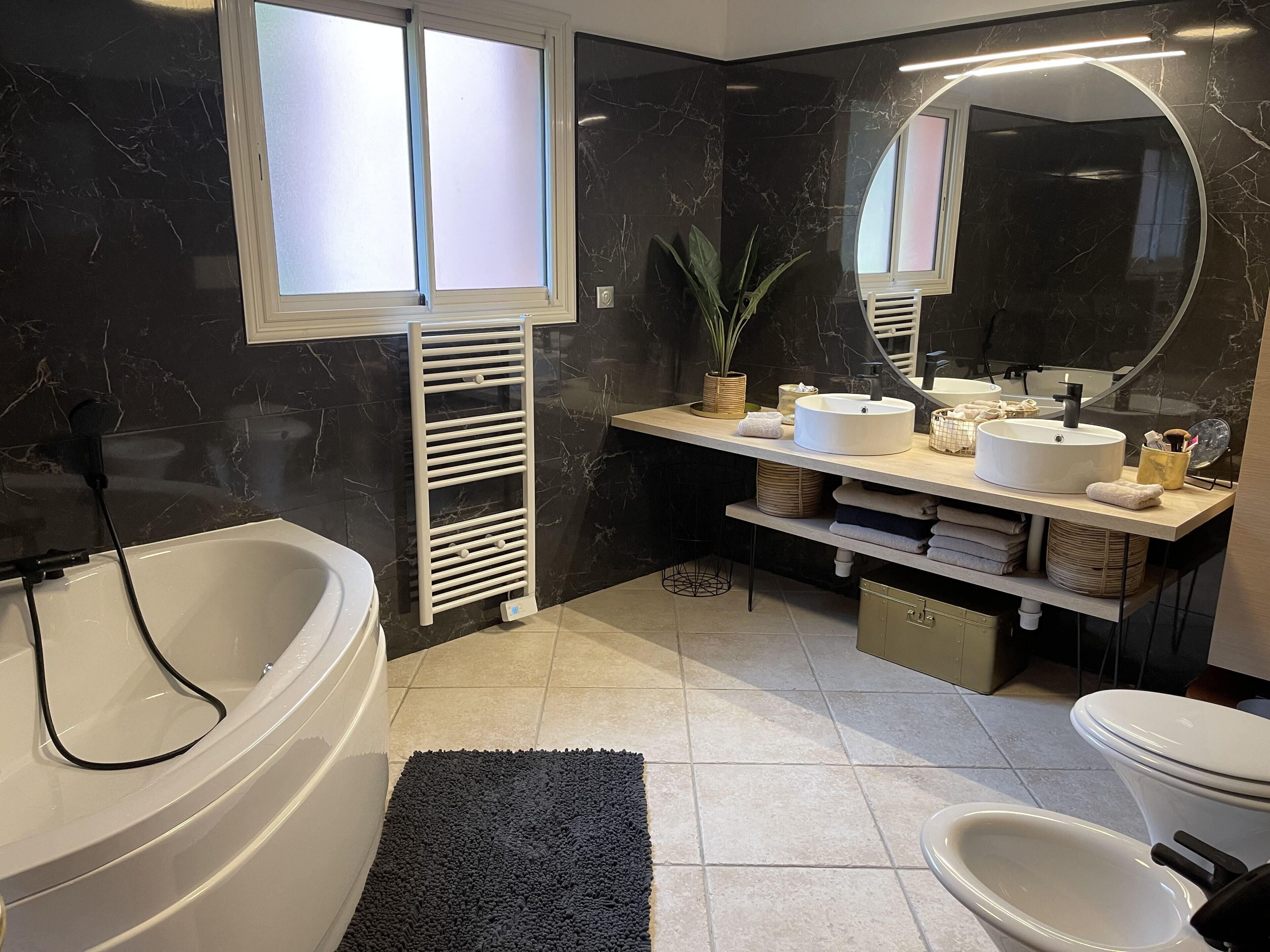Un baño moderno con una bañera independiente, un tocador con lavamanos redondo, un espejo grande y una pared de mármol negro.