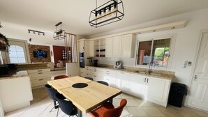 A modern kitchen with white cabinets, a wooden dining table, and black chairs. - 3 bedroom Villa in Porticcio with Sea view (PORTICCIO)