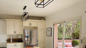 A modern kitchen with white cabinets, a wooden dining table, and a black pendant light. - 3 bedroom Villa in Porticcio with Sea view (PORTICCIO)
