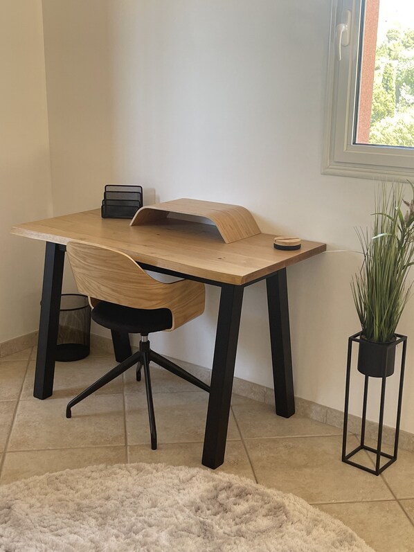 A modern office desk with a wooden surface and black metal legs, accompanied by a black office chair. A small potted plant is placed beside the desk.