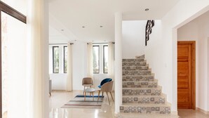 Un interior moderno con una escalera, una puerta de madera y un área de descanso con sillas.