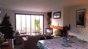 Een woonkamer met een bank, een eettafel en een televisie. Er is een schuifdeur die leidt naar een terras.