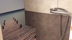 Douchegedeelte met een houten bankje, douchekop en afvoer.